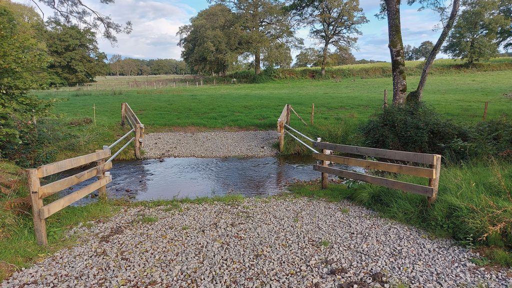 Photo d'un petit cours d'eau. Des barrières et des clôtures limitent l'accès du bétail au lit de la rivière. La zone de passage est stabilisée pour éviter les effets d'érosion liés aux piétinement des animaux.
