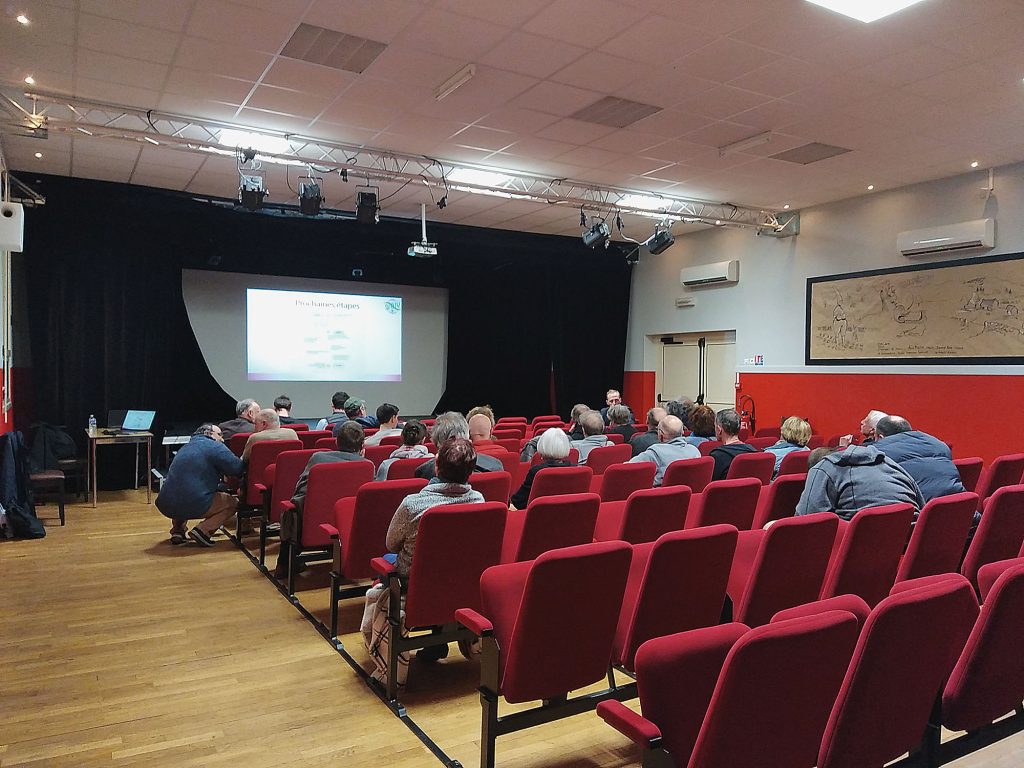 Salle de réunion à Blond. Un public assis fait face à un écran diffusant une présentation.